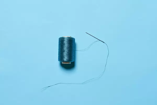 A spool with blue thread and sewing needle on blue background