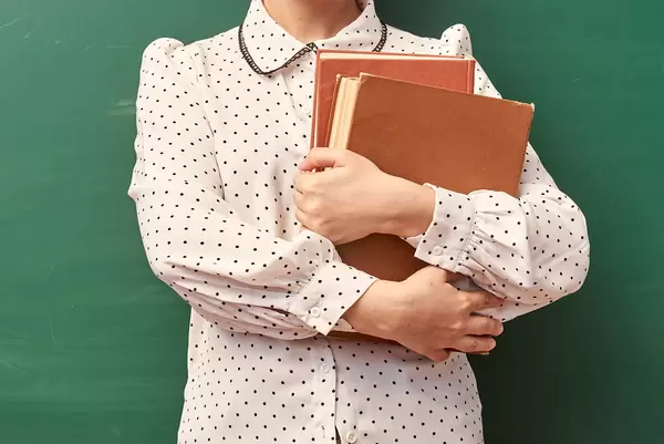A teacher holding in hands two books and posing over green chalkboard
