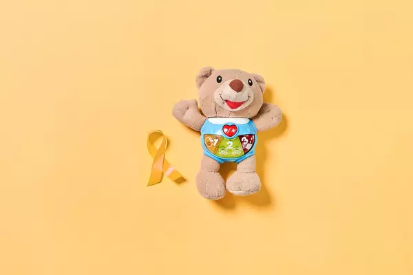 A teddy bear with childhood cancer awareness yellow ribbon. February, 15 - Childhood Cancer Day