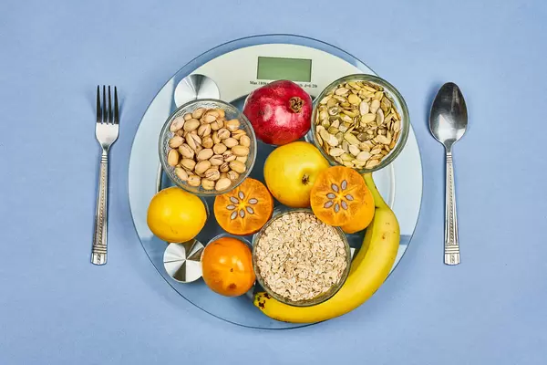 A weight scale full of different dieting fruits, nuts and pumpkin seeds