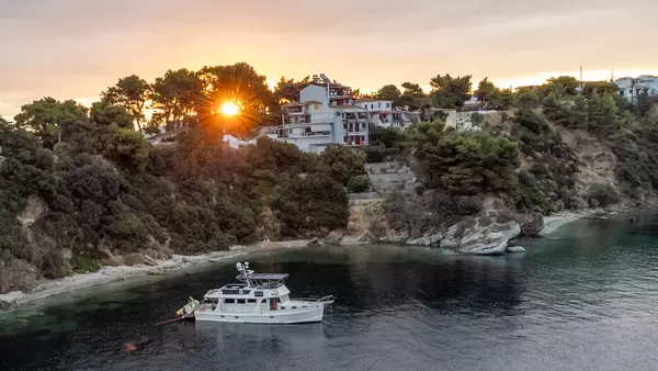 A white boat at sunset in front of the houses on the rocky coast of Skiathos, Thessaly