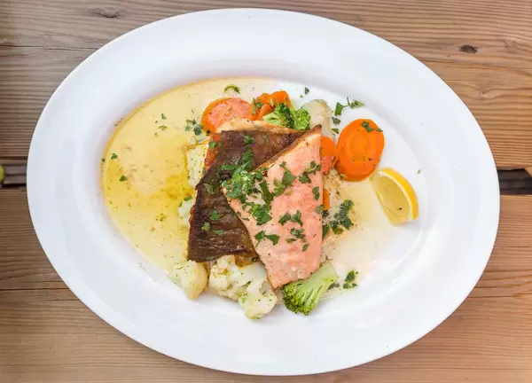 A white plate with char, cauliflower, broccoli, carrot and herbs. Typical fish from the Alpine lakes