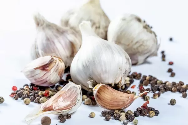 A whole head of garlic and cloves with a tooth of pepper peas on a white background