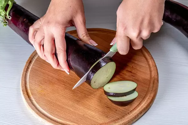 A woman cuts an eggplant with a knife on the kitchen Board (Flip 2019)