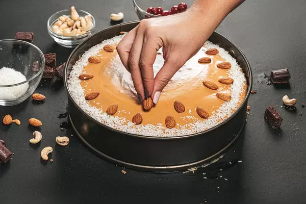A woman decorates the cake with almonds. Birthday preparations