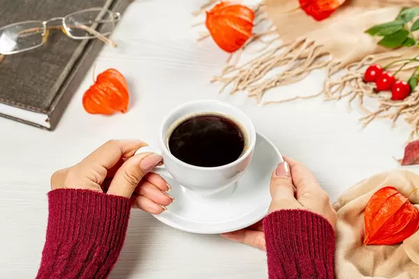 A woman holding a Cup of coffee on the table is a book and glasses. The concept of rest in the autumn season (Flip 2019)