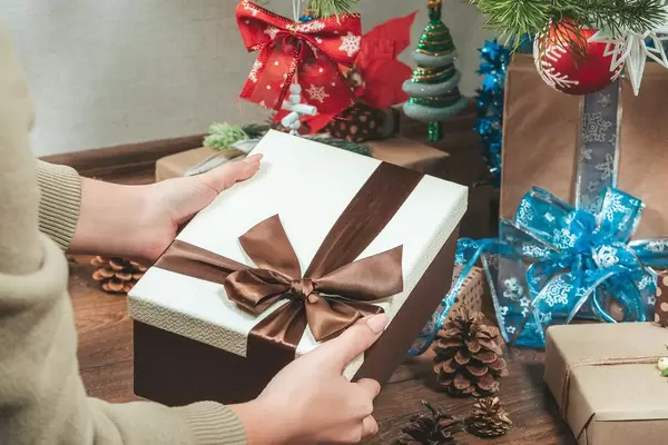 A woman holds a gift box under a Christmas tree