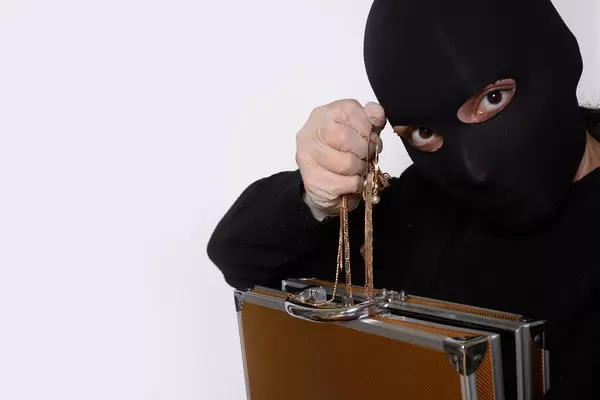 A woman in a black face mask taking golden gems from a suitcase and showing stolen gold jewelry
