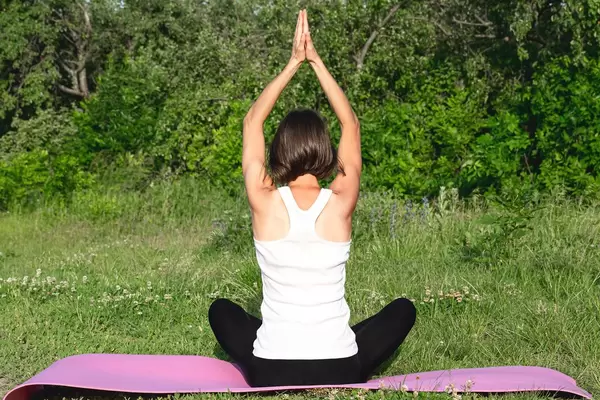 A woman is meditating in a half-nose pose with her arms above her head - Sanjali padmasana. Back view