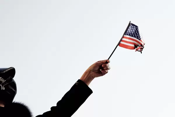 A woman participating in protests in Washington DC standing on the street holding a burning USA flag under the blue sky