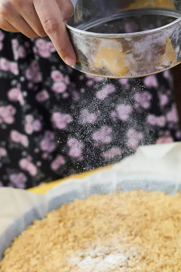 A woman pouring powdered sugar on a freshly baked cottage cheese pie