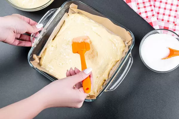A woman spreads the dough in a baking tray with a kitchen spatula