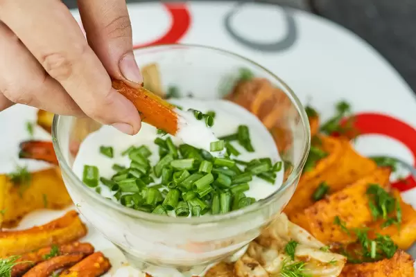 A woman tasting pumpkin chips. Dipping fried pumpkin slice to the sauce