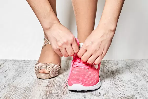 A woman tired after wearing high heels putting on comfortable sporty sneakers