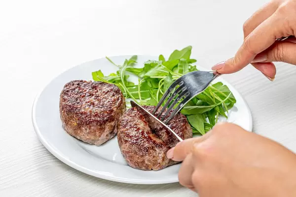 A woman with a knife and fork in her hands cuts a meat cutlet (Flip 2019)