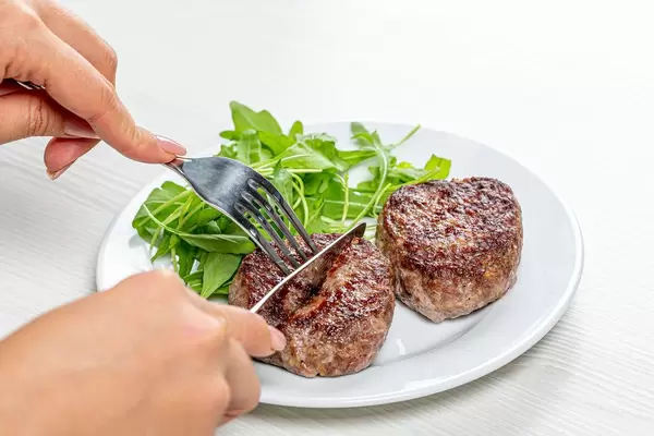 A woman with a knife and fork in her hands cuts a meat cutlet