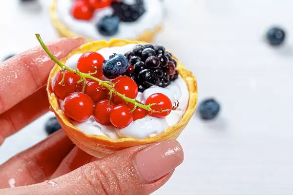 A woman's hand holding a cake with berries and cream. Close up