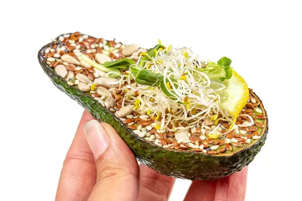 A woman's hand holds half an avocado with seeds and micro greens