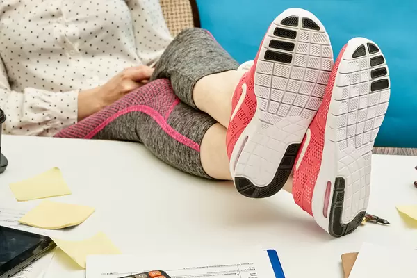 A worker in sport wearings hanged legs on a working desktop with documents and office supplies