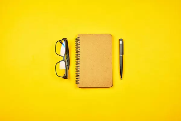 A writer's workspace. Notepad with eyeglasses on yellow background