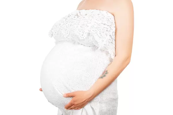 A Young beautiful woman standing in white dress holding her big belly with two hands