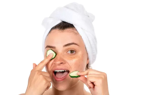 A young woman with a towel on her hair and pieces of fresh cucumbers. The concept of beauty