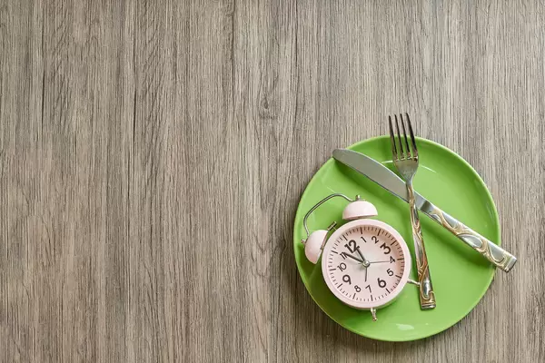 Ab in die Mittagspause! Geschirr und Wecker vor einem hölzernen Hintergrund. Aufnahme von oben