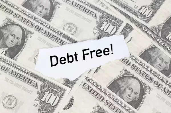 Abgerissener Notizzettel mit dem Text "Debt Free!" (Schuldenfrei) auf amerikanischen einhundert Dollar-Scheinen