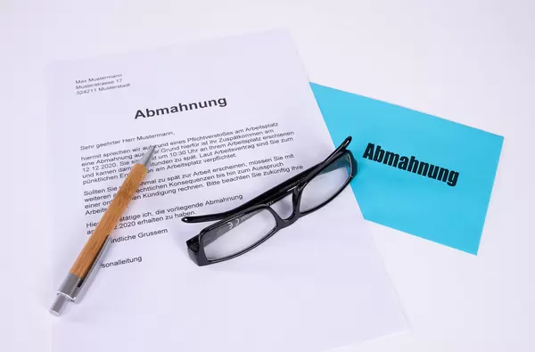 Abmahnung document with pen, glasses and blue envelope on white table