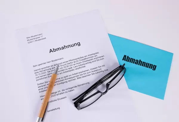 Abmahnung document with pen, glasses and envelope on white table