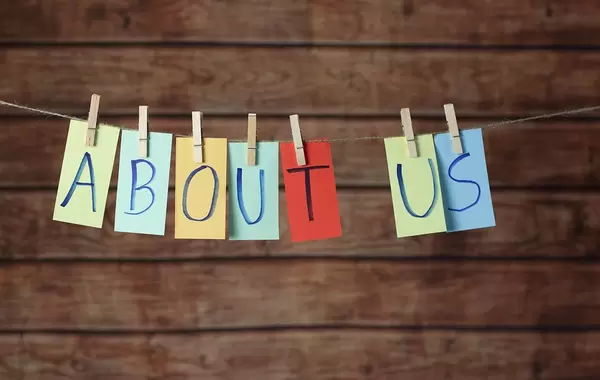 About us on paper hanging with clothespins on a rope infront of a wooden background