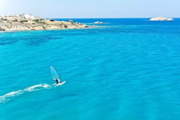 Active holiday in Greece: windsurfer by the headland of Mikri Vigla in the blue waters of Naxos