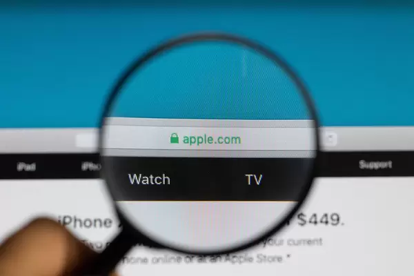 Adresse der Apple Internetseite "apple.com", vergrößert unter einem Lupenglas dargestellt