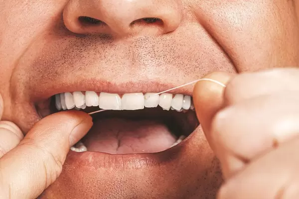 Adult man cleaning flossing his white teeth with dental floss