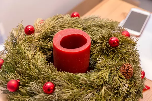 Adventskranz mit einer, teilweise abgebrannten, Kerze und roten Weihnachtskugeln vor Smartphone