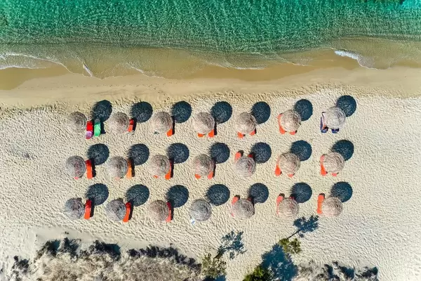 Aerial photo: geometry on Plaka beach on Naxos. Three rows of straw parasols, dunes and sea