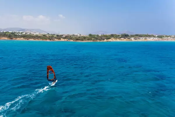Aerial shot of a man windsurfing in the Aegean Sea, with the coast of Paros in the background