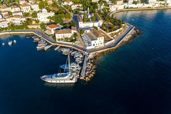 Aerial view of an anchored luxury yacht and fisher boats in the old harbour of the Argosaronic island Spetses, Greece, in front of church Agios Nikolaos