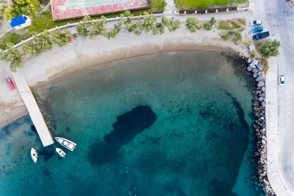 Aerial view of bay with pier and three boats, beach, blue sea and road with parked cars in Milos, Greece