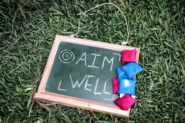 AIM WELL written on a chalkboard with tossing bags on the side