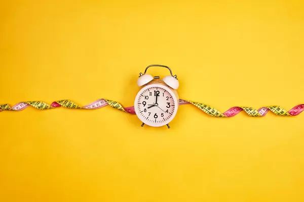 Alarm clock and measuring tape on yellow