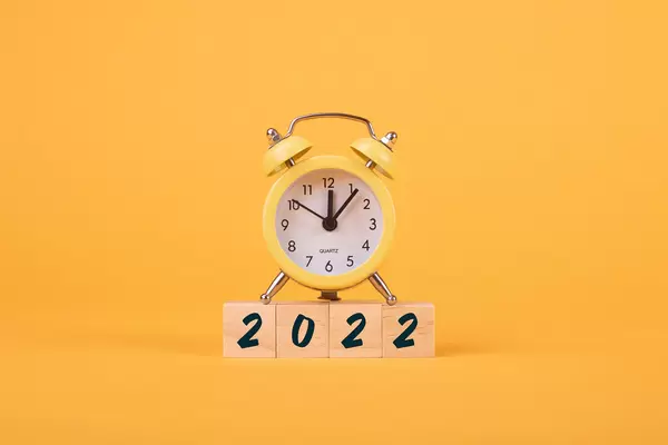 Alarm clock and wooden blocks with 2022 text on yellow background