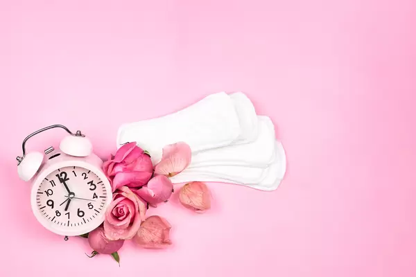 Alarm clock, sanitary pads and beautiful roses on a bright pink background
