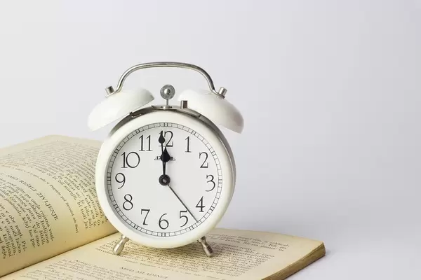 Alarm Clock showing almost midnight and standing on an open book on white background