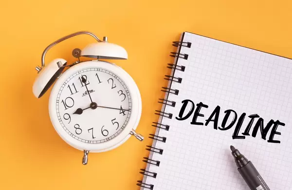Alarm clock with handwritten Deadline text on yellow background