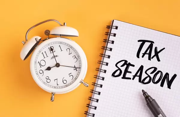 Alarm clock with handwritten Tax Season text on yellow background