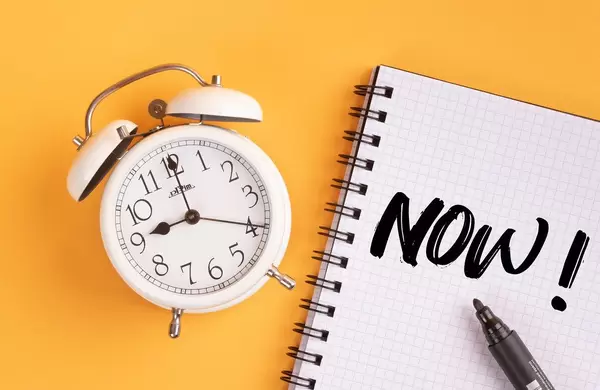 Alarm clock with handwritten text Now! on yellow background