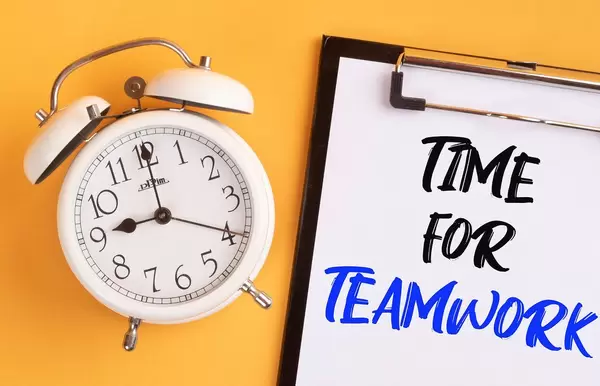 Alarm clock with handwritten text Time for Teamwork on clipboard