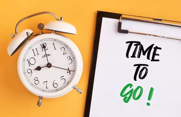 Alarm clock with handwritten text Time to Go on clipboard