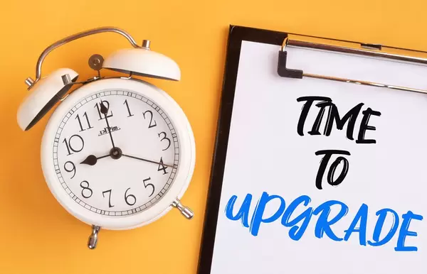 Alarm clock with handwritten text Time to Upgrade on clipboard